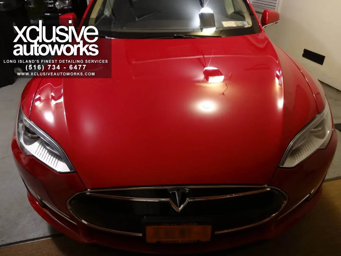 A red tesla model s is parked in a garage by xclusive autoworks