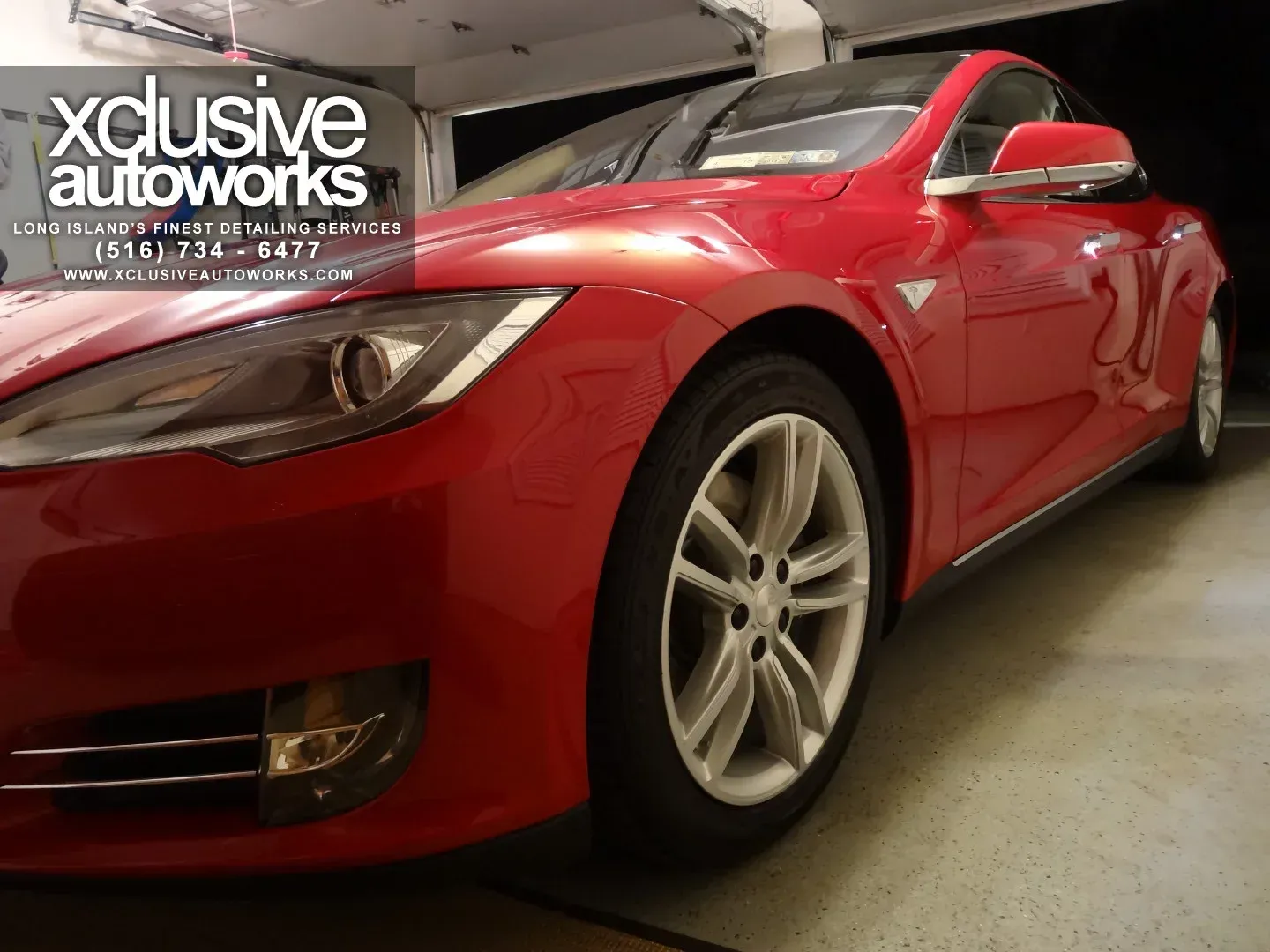 A red tesla model s is parked in a garage by xclusive autoworks