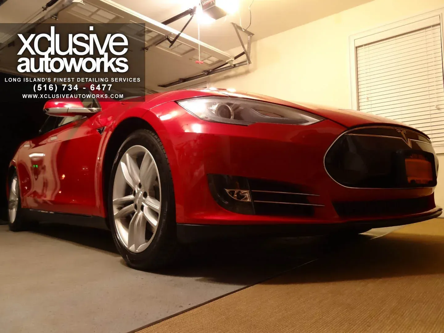 A red tesla model s is parked in a garage.