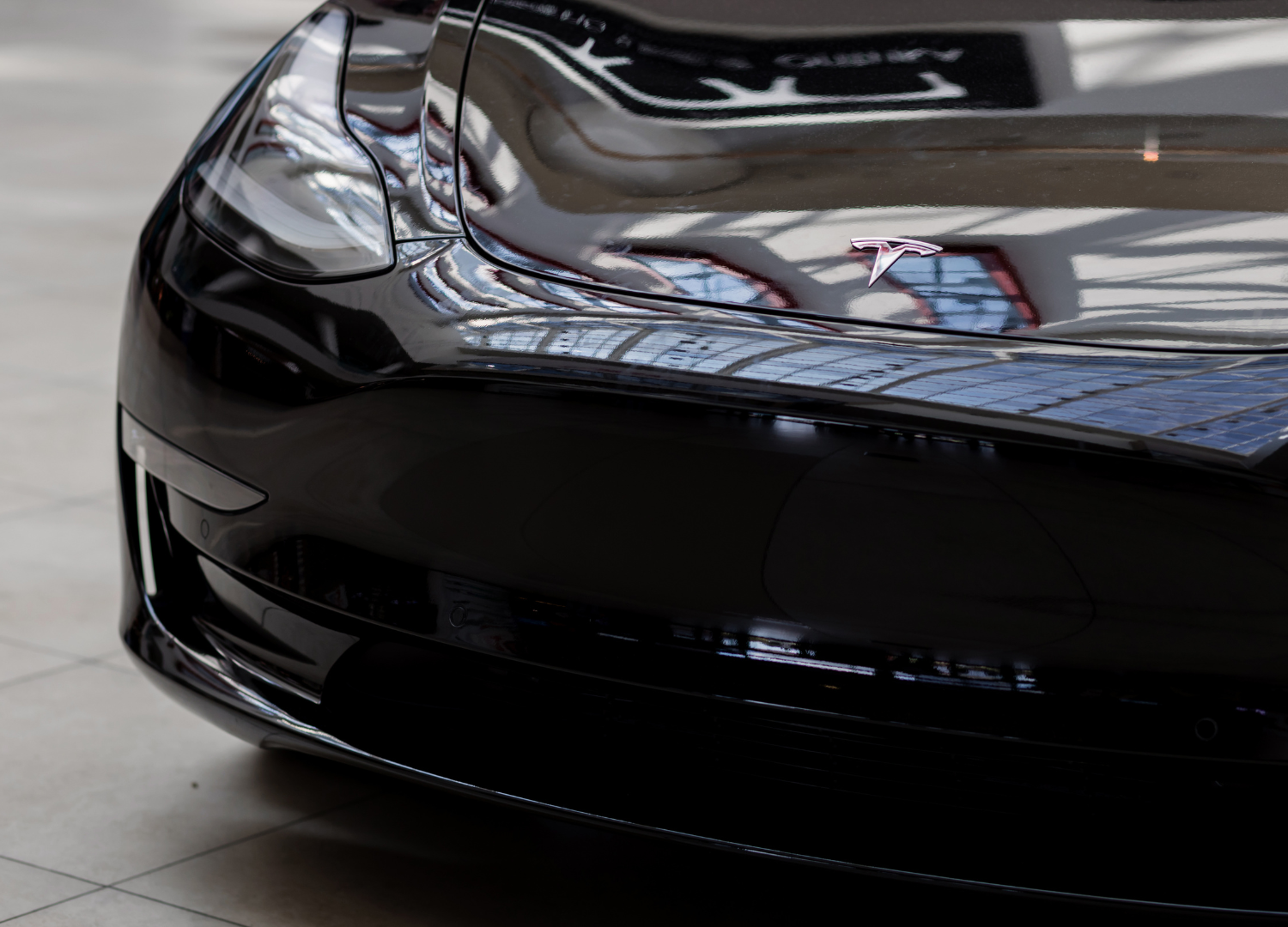 A black tesla model 3 is parked on a concrete floor.