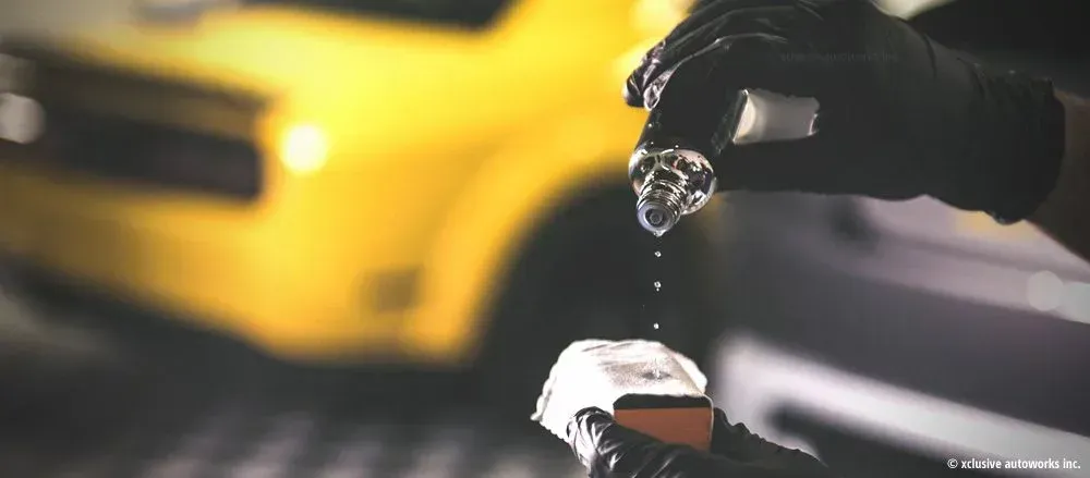 A person wearing black gloves is holding a small object in front of a yellow car.