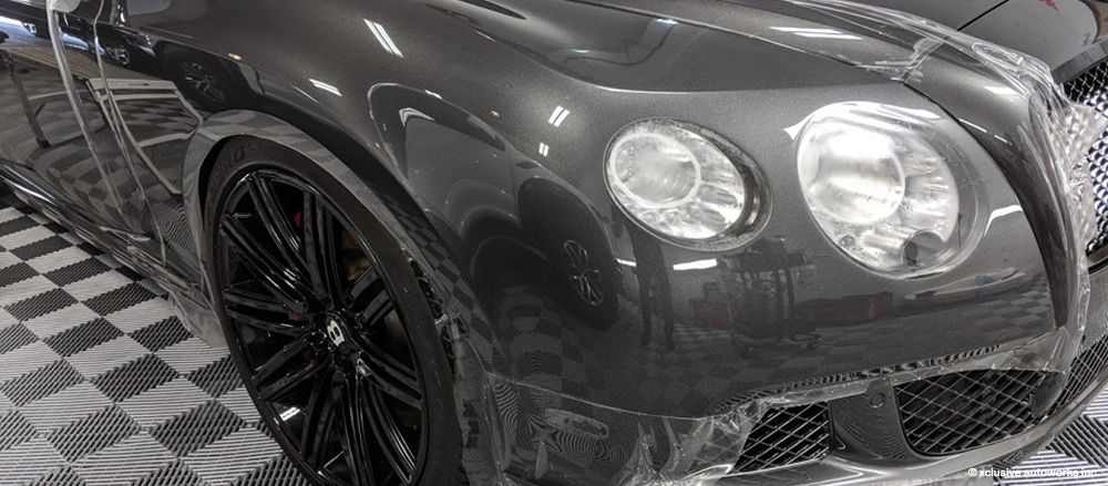 A bentley continental gt is wrapped in plastic and sitting on a checkered floor.