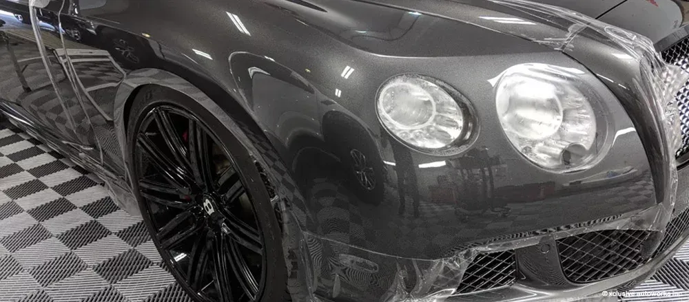 A man is cleaning the hood of a black car with a cloth.