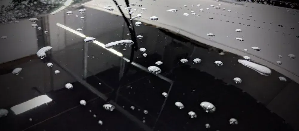 A black car with water drops on the hood and windshield.