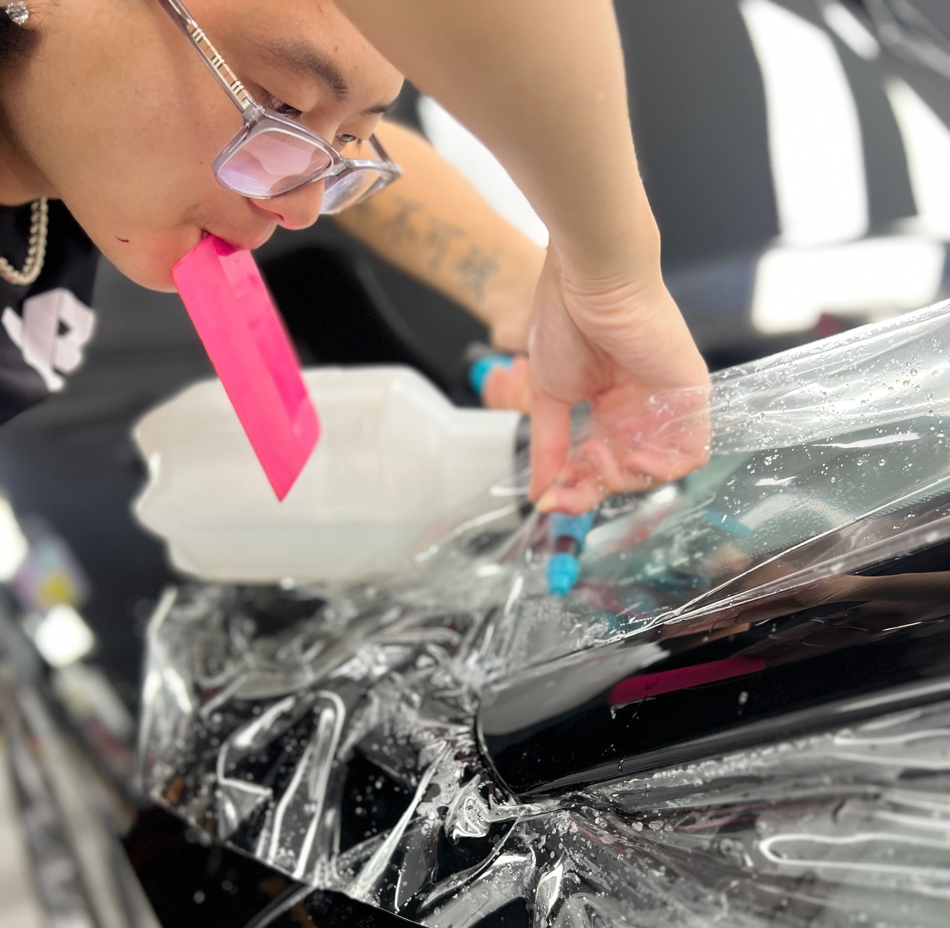 A woman wearing glasses is wrapping a car with plastic wrap