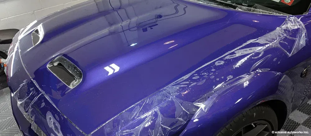 The hood of a purple car is wrapped in plastic.