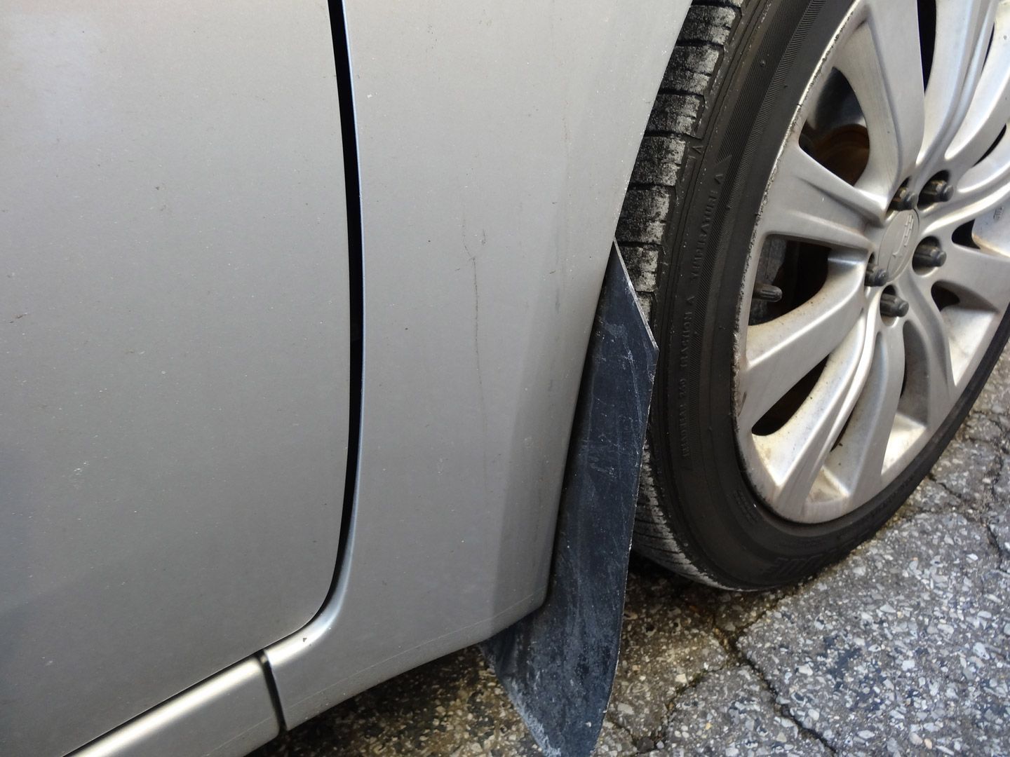 A silver car with a blue mud flap on the side of it.