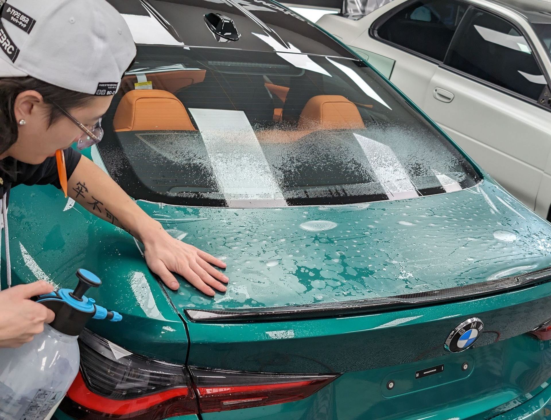 A woman is spraying water on a green car.