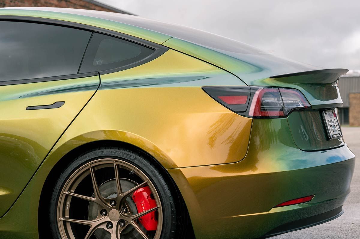 A tesla model 3 is painted in a rainbow of colors and has a red brake caliper.