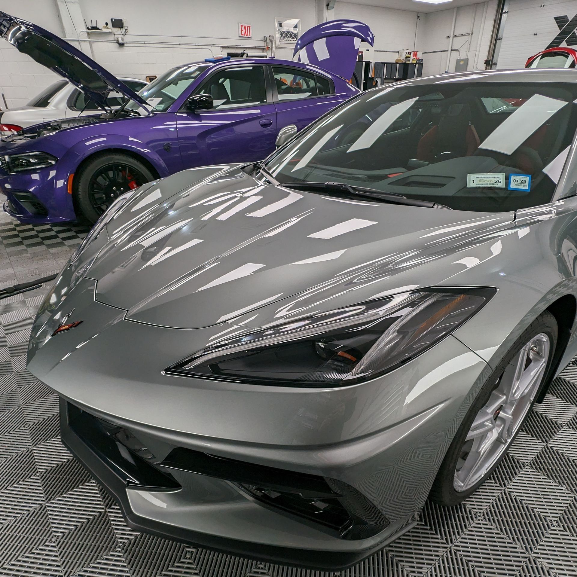 A gray sports car is parked next to a purple sports car in a garage.