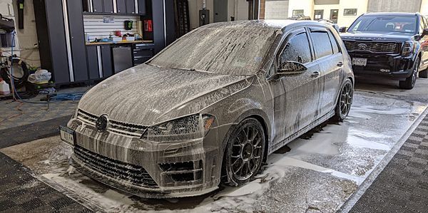 A dirty car is covered in foam in a parking lot.