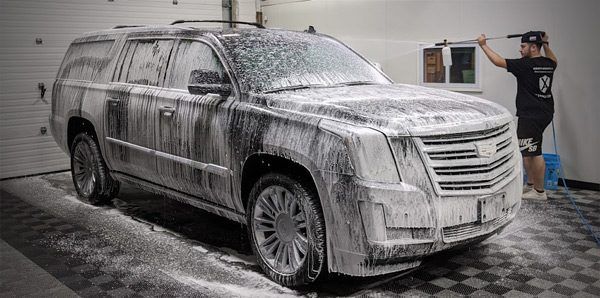 A man is washing a car with foam in a garage.