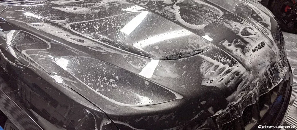 A black car is being washed with soap and water in a garage.