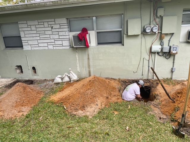 A man is digging a hole in the ground in front of a house.