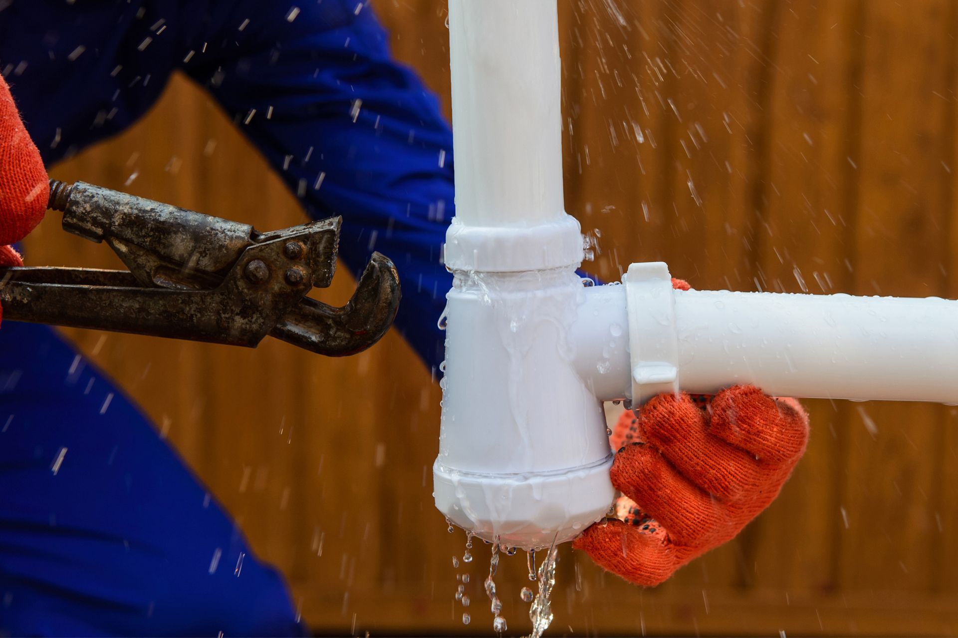 A plumber is fixing a leaking pipe with a wrench.