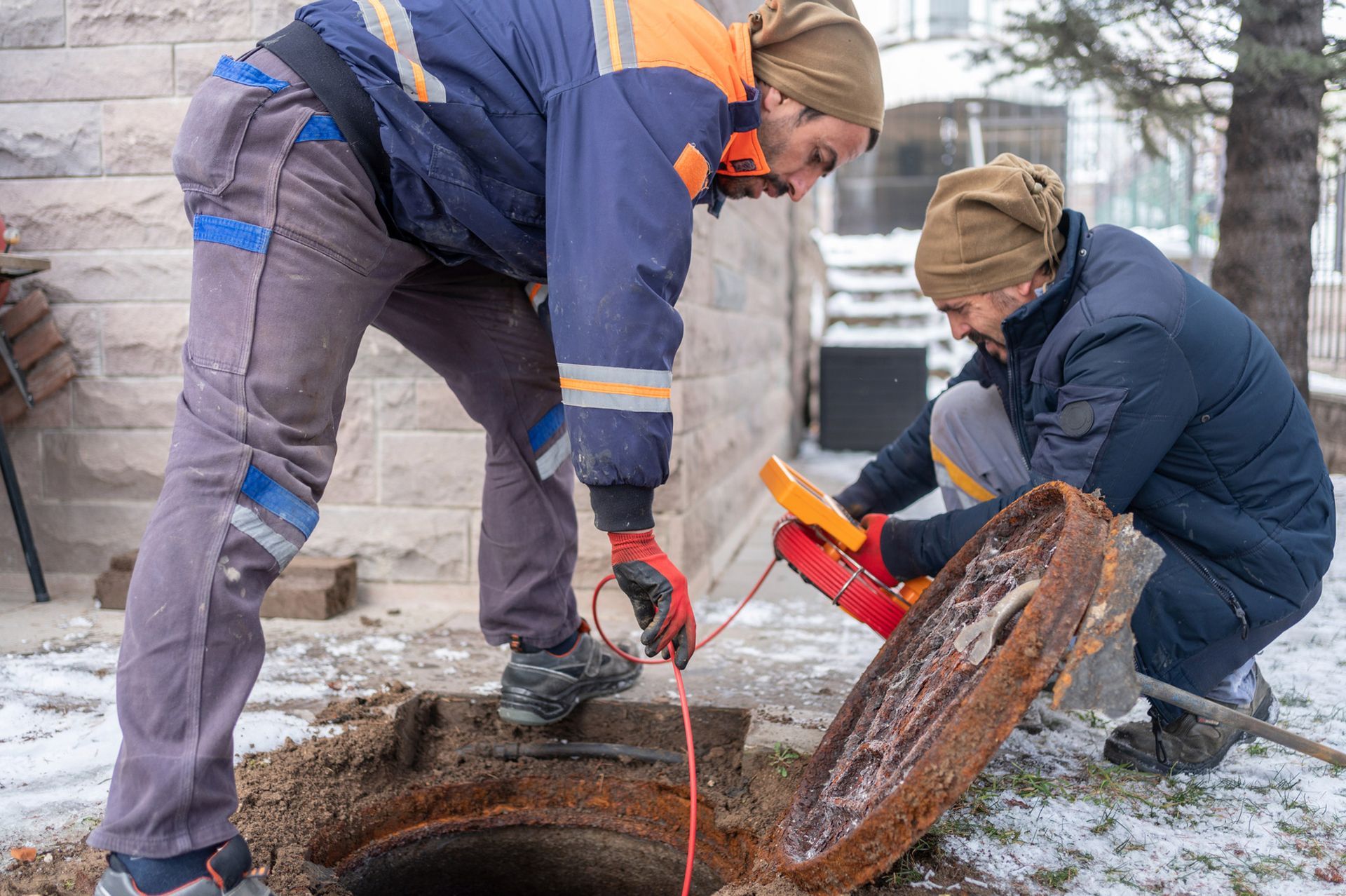 Two men are working on a manhole cover in the snow.