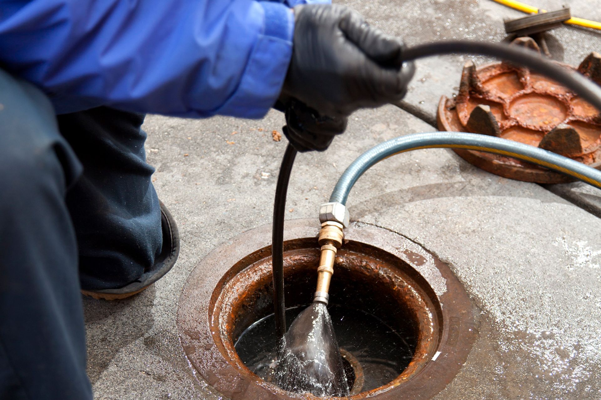 A man is cleaning a manhole with a hose.