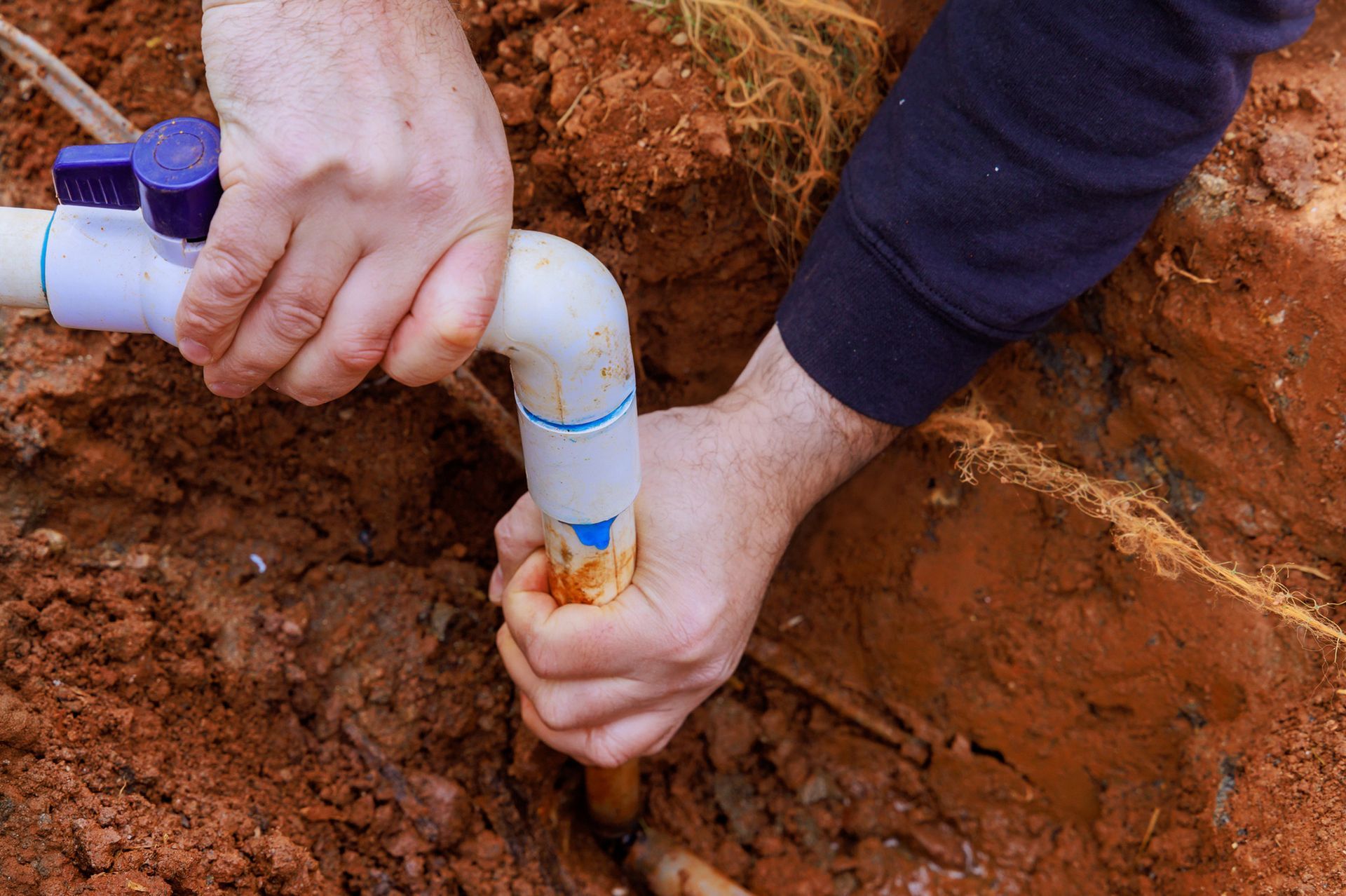 A person is fixing a pipe in the dirt.