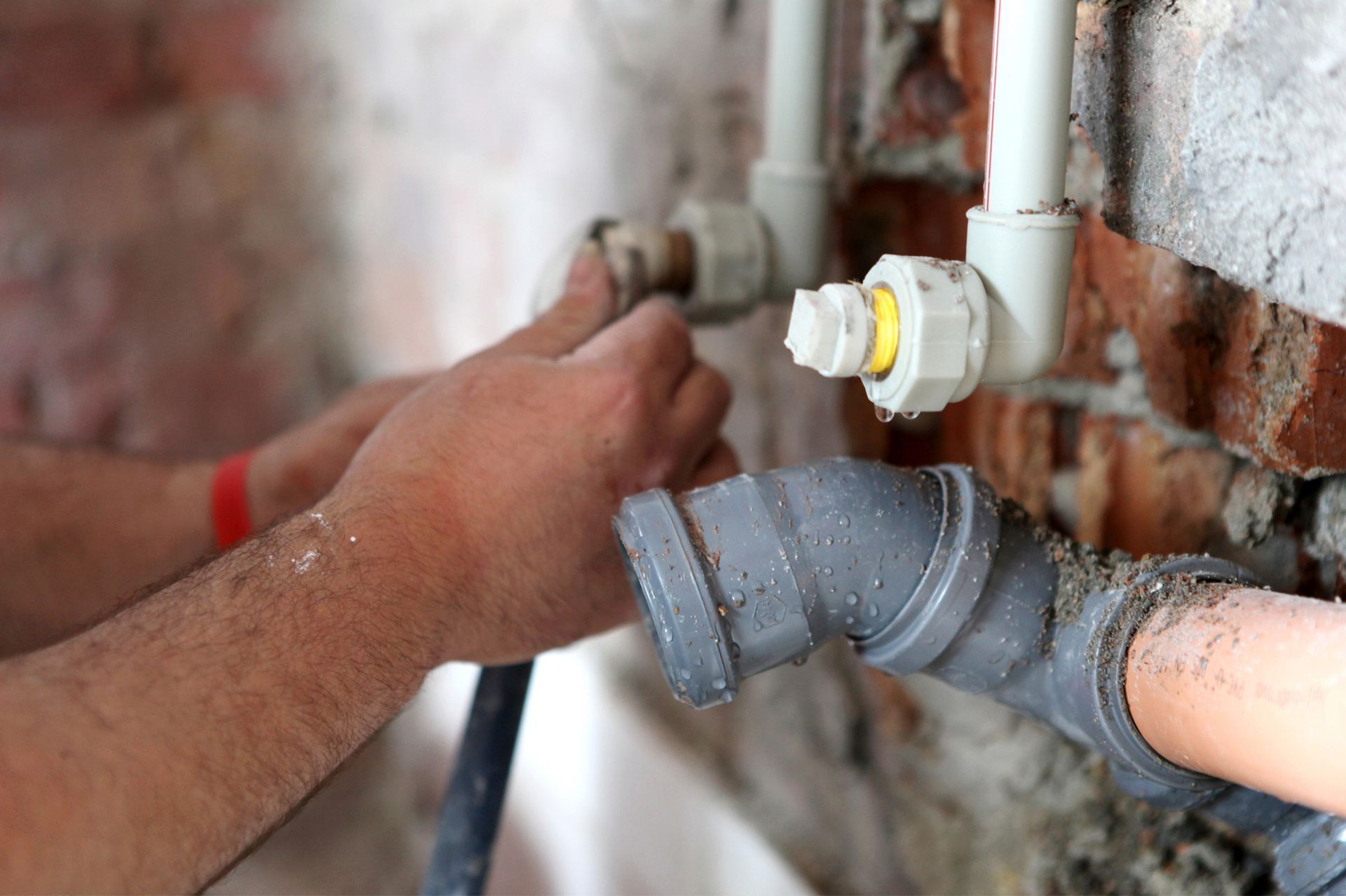 A man is fixing a pipe in a brick wall.