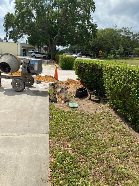 A cement mixer is sitting on the side of the road next to a hedge.