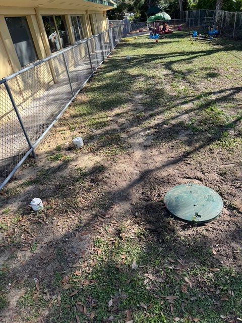 A backyard with a fence and a septic tank in the middle of it.