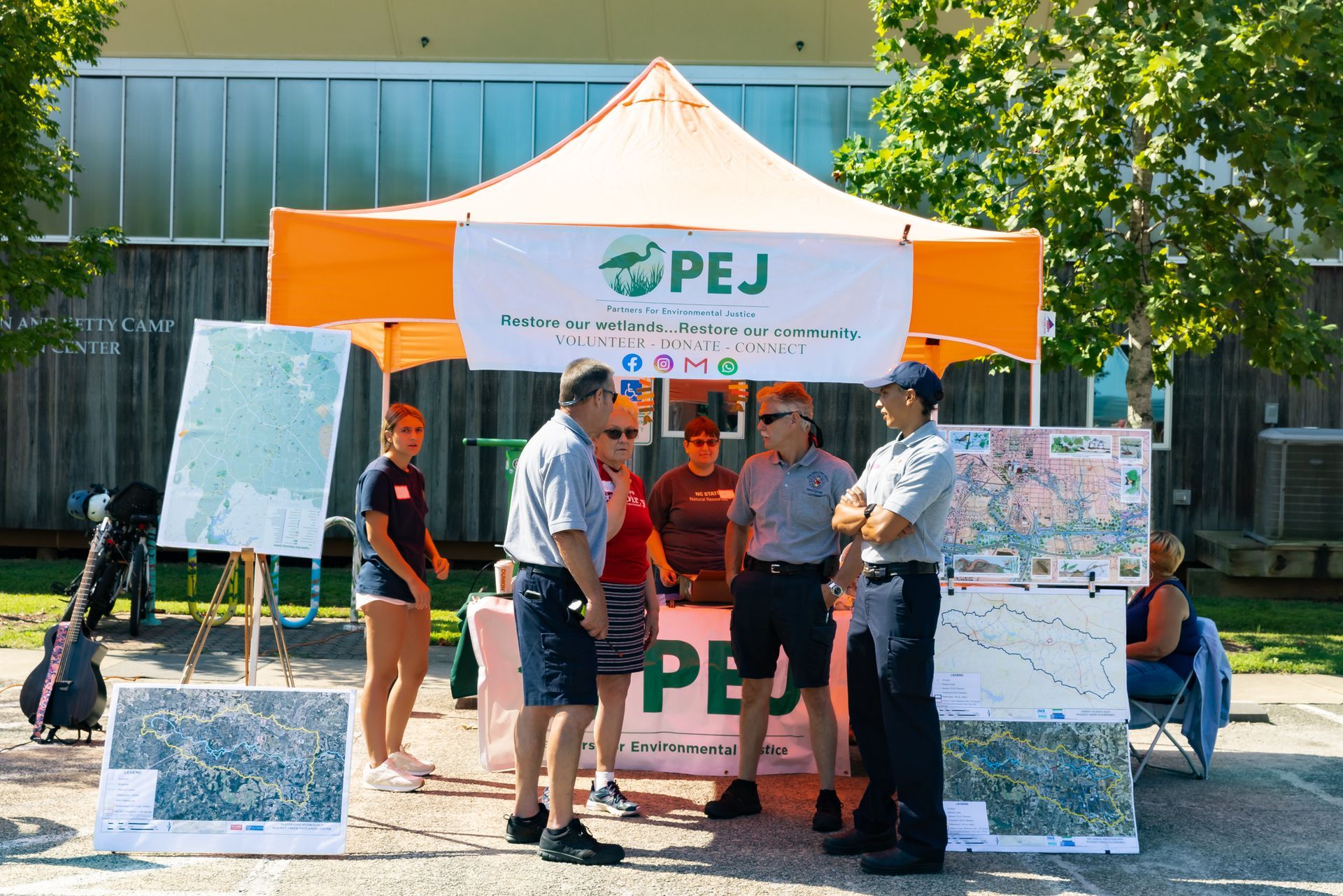 A group of people are standing under an orange tent that says pej