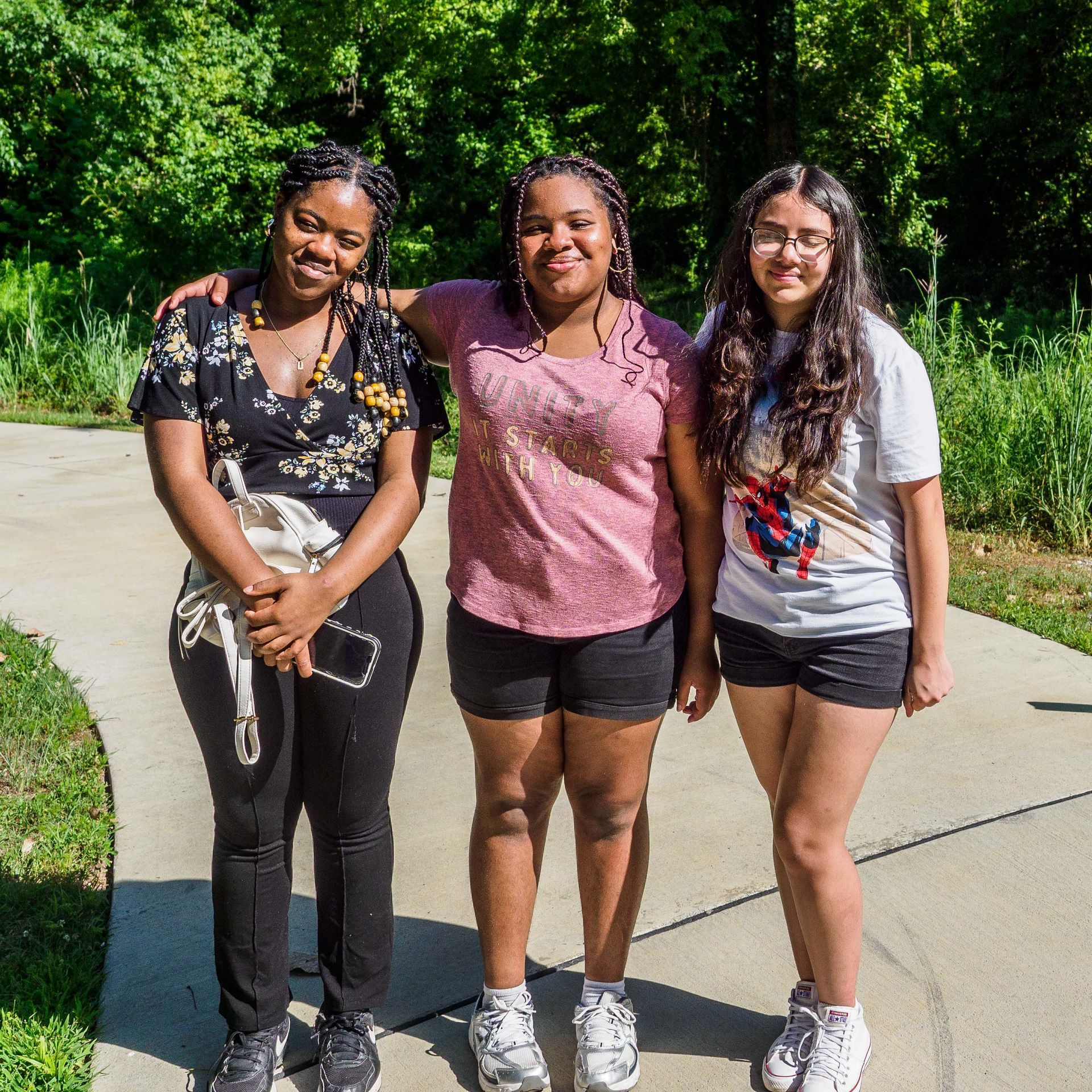 Three young women are posing for a picture on a sidewalk