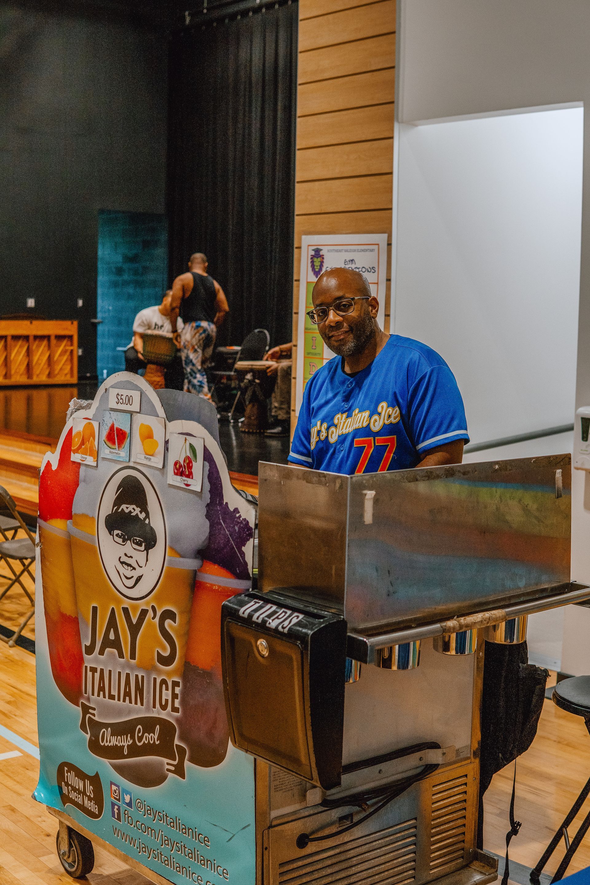 A man is standing in front of a jay 's italian ice cart.