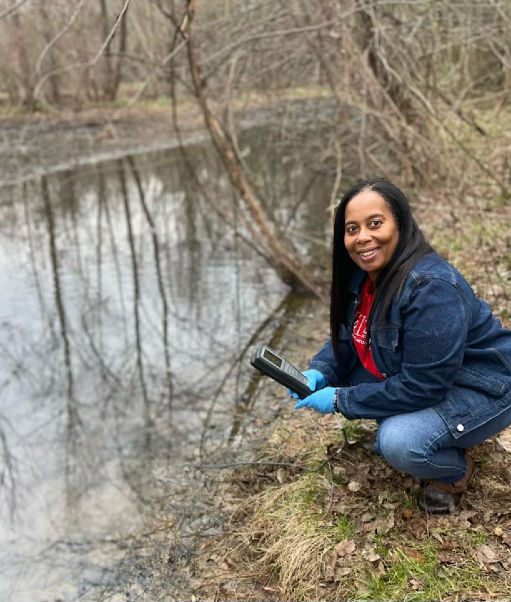 A woman is kneeling next to a body of water holding a tablet.