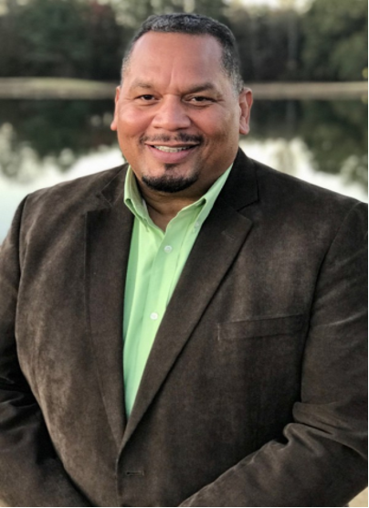 A man in a suit and green shirt is smiling for the camera