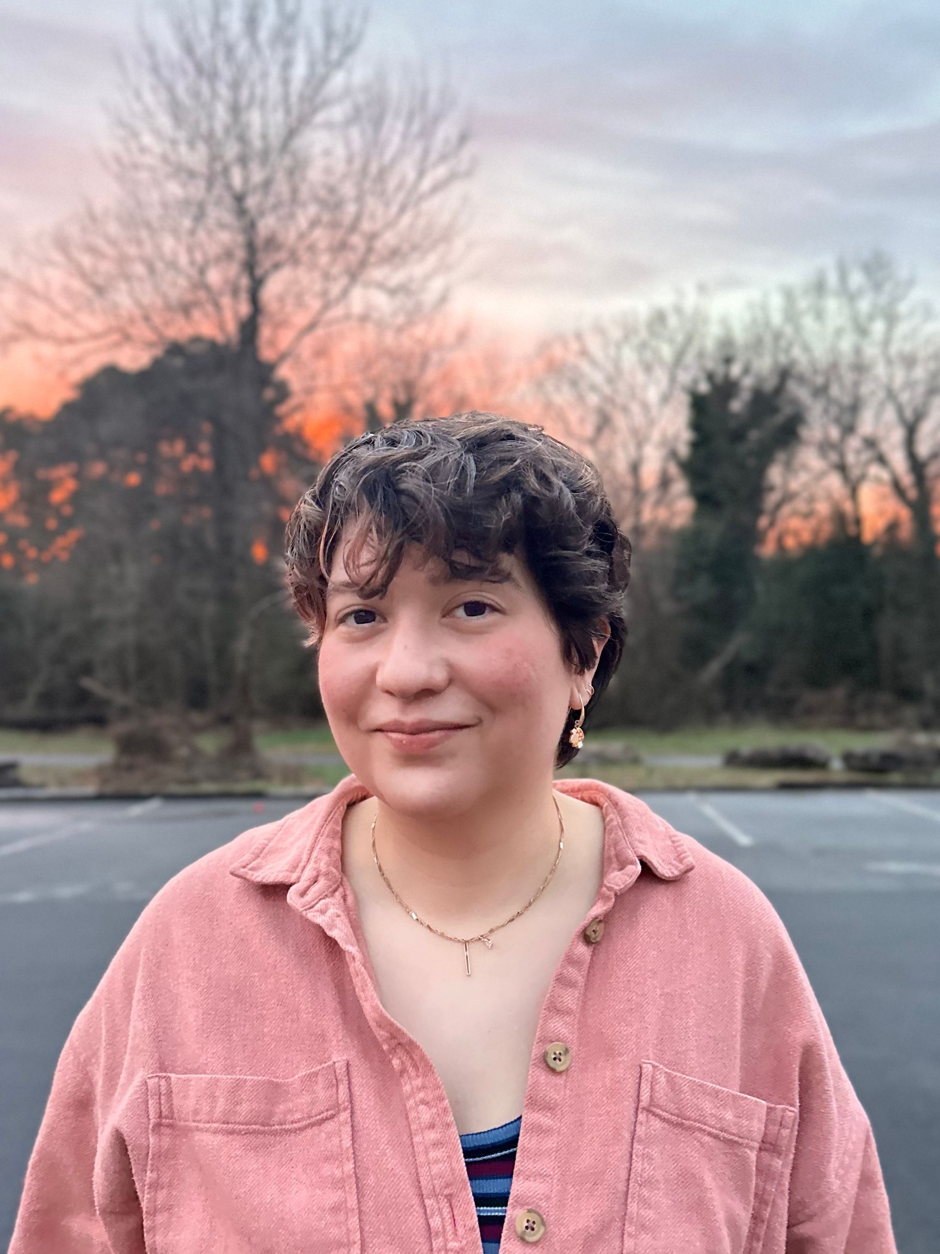 A woman in a pink shirt is standing in a parking lot.