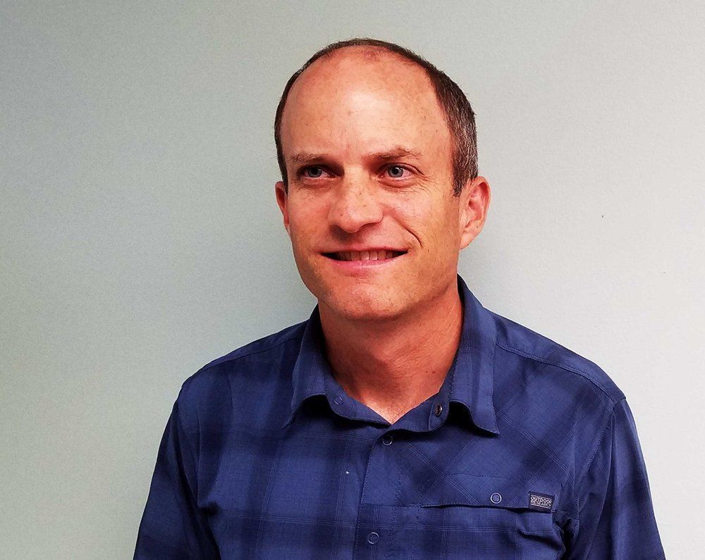 A man in a blue plaid shirt is smiling for the camera.