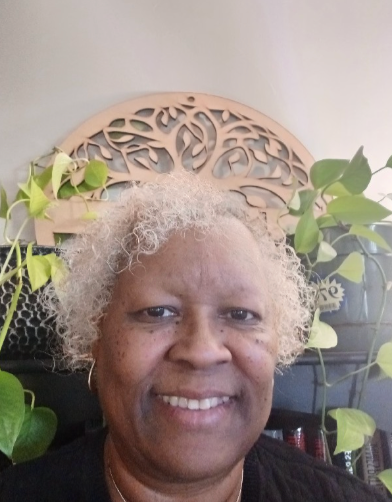 A woman with white hair is smiling in front of a wooden tree.