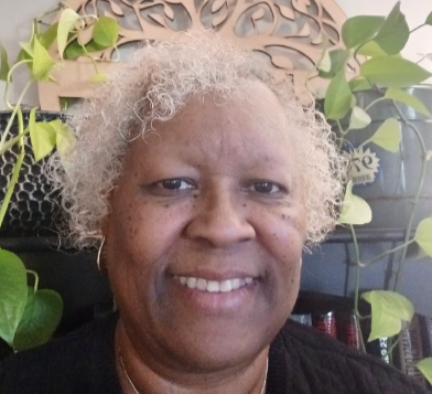 A woman with white hair is smiling in front of a wooden tree.