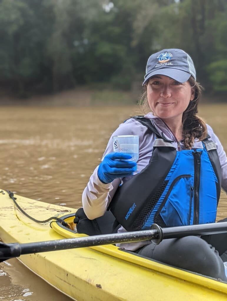A woman is sitting in a kayak holding a cup of coffee.