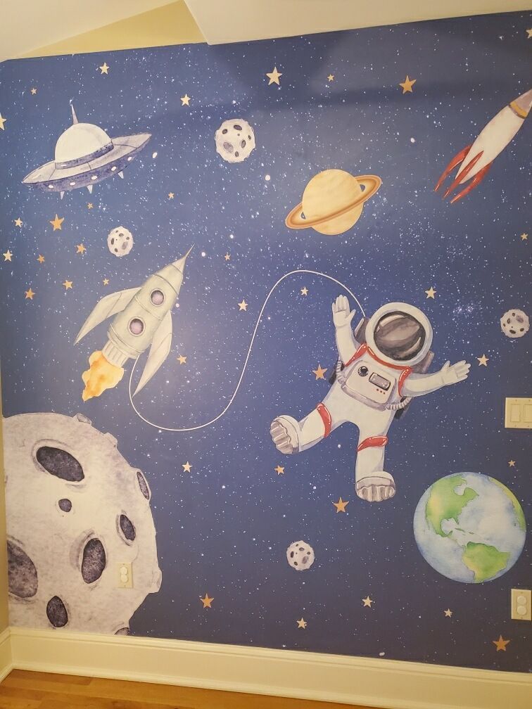 A wall with a mural of an astronaut , rockets , planets and stars.