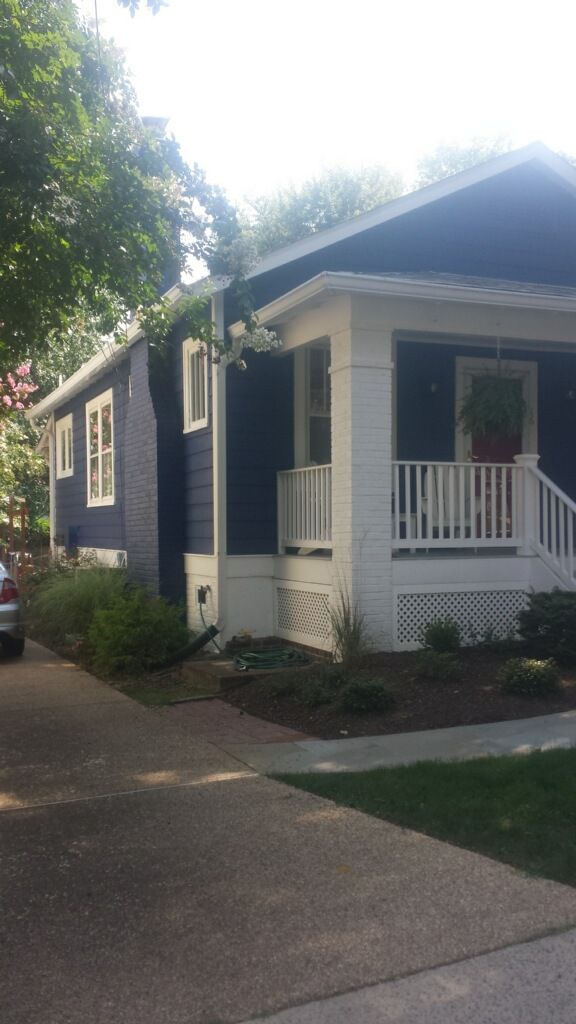 A blue house with a white porch and a car parked in front of it.