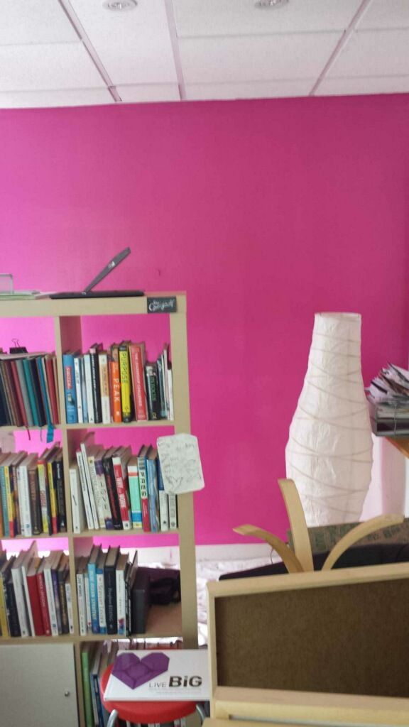 A room with a pink wall and a shelf full of books