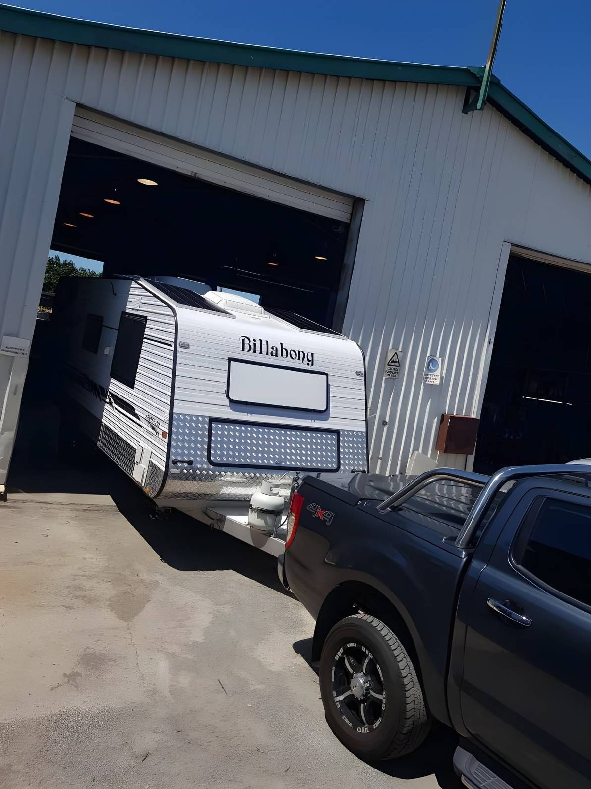 A Caravan Being Towed Out of a Garage by a Dark Gray Pickup Truck on a Sunny Day — Shannon's Auto Electrical in Garbutt, QLD