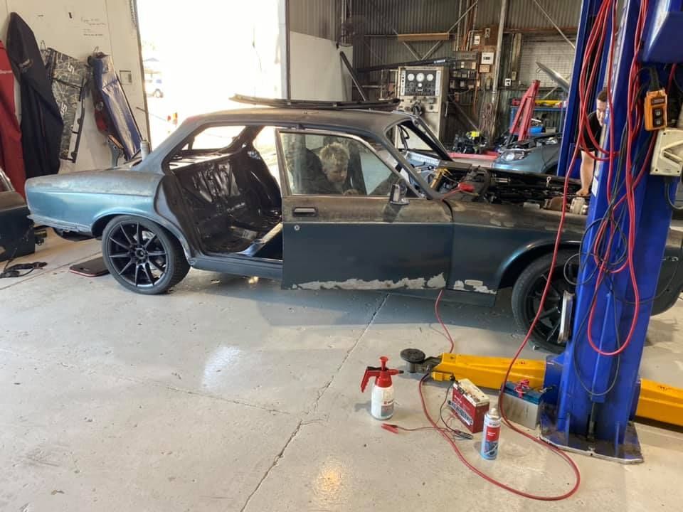 A Partially Dismantled Teal Car Inside a Garage Sits on a Lift. the Driver's Door is Open, and the Interior is Exposed — Shannon's Auto Electrical in Garbutt, QLD
