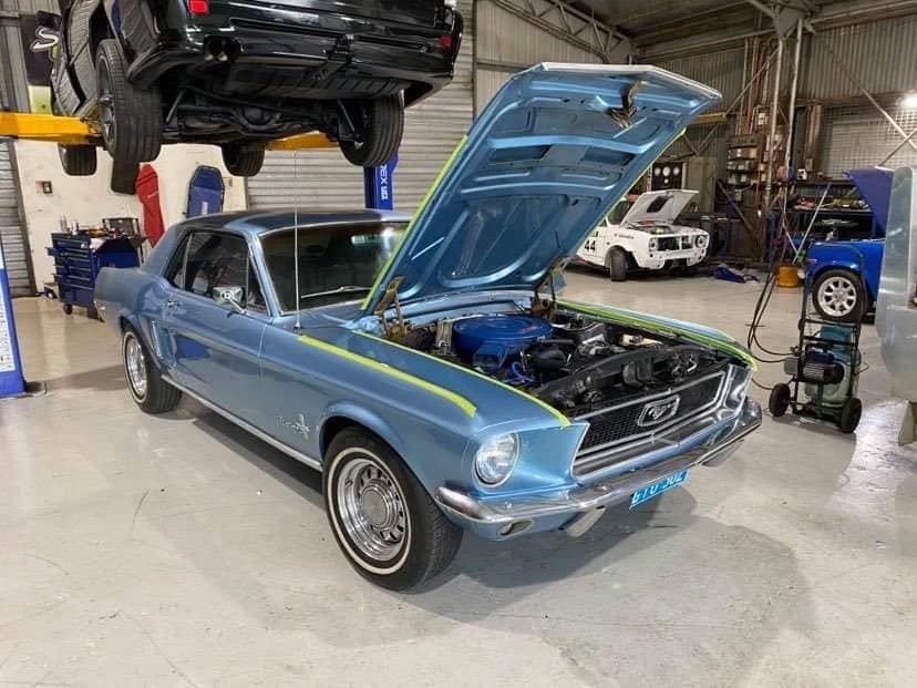 A lIght Blue Classic Ford Mustang With Its Hood Open in a Garage. a Black Vehicle is Hoisted Above — Shannon's Auto Electrical in Garbutt, QLD