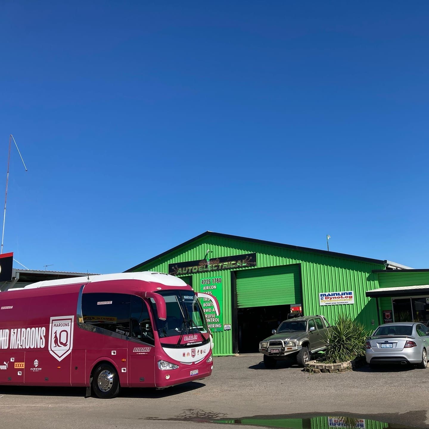 A Maroon Bus With Logos Parked in Front of an Auto Electrical Shop With a Green Exterior. Blue Sky Overhead — Shannon's Auto Electrical in Garbutt, QLD