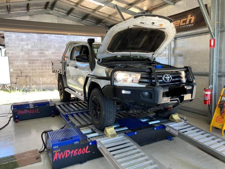 A White Toyota Truck on a Dynamometer With Its Hood Open. It is in a Workshop Setting With Equipment — Shannon's Auto Electrical in Garbutt, QLD