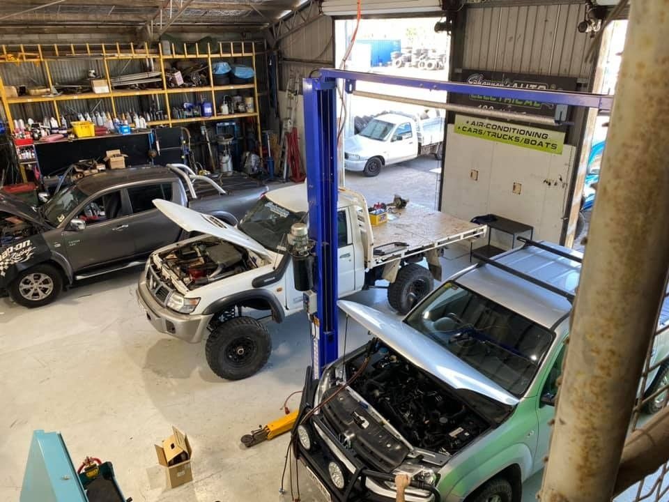 An Auto Repair Shop With Multiple Vehicles Being Worked on, Including a Lifted White Suv and a Green Truck. Tools and Equipment Are Visible Throughout the Shop — Shannon's Auto Electrical in Garbutt, QLD
