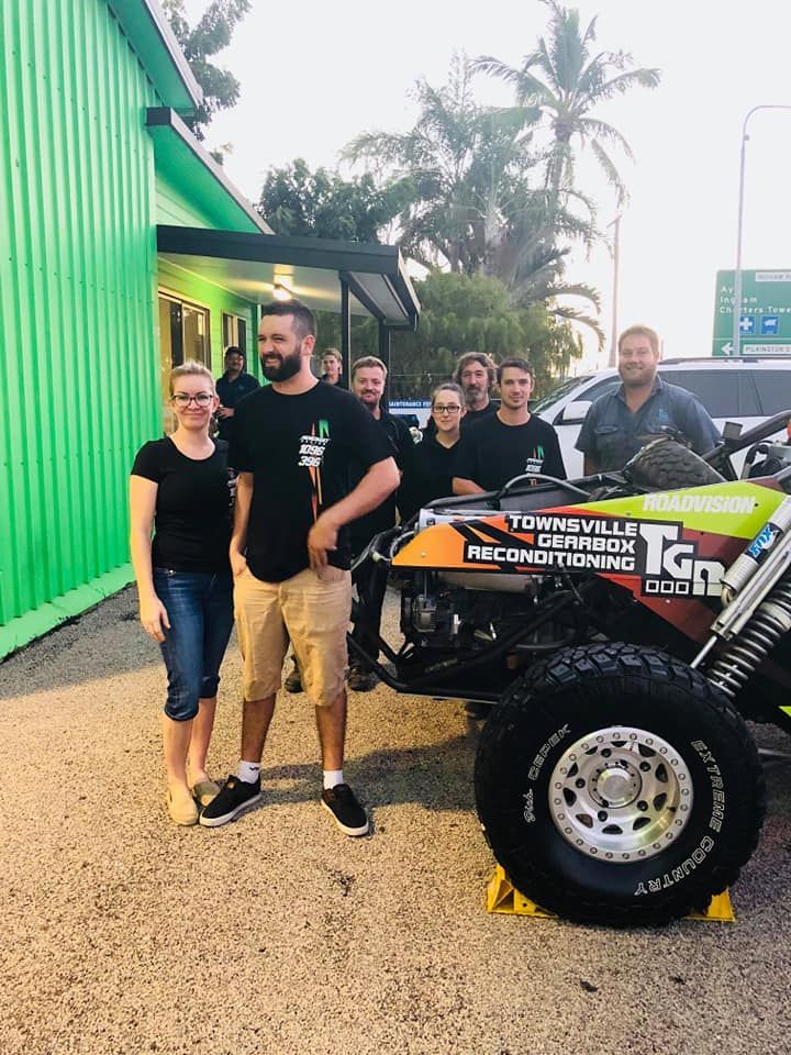 Group of People Posing With a Custom Buggy in Front of a Green Building. the Buggy Has the Words 