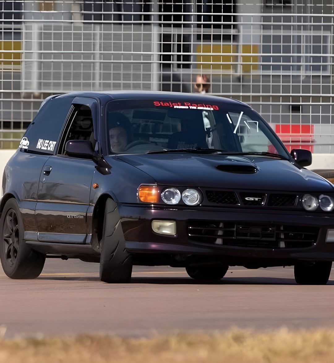 Dark Purple Toyota Starlet Racing on a Track With a Driver. It Has Black Wheels and a Hood Scoop — Shannon's Auto Electrical in Garbutt, QLD
