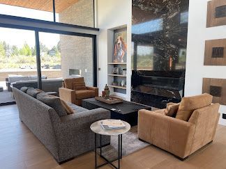 Modern living room with gray and tan sofas, fireplace, and large windows overlooking outdoors