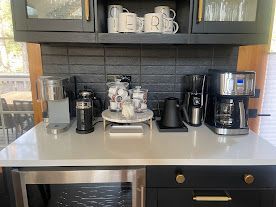 Modern kitchen coffee station with mugs, espresso machines, and a coffee maker on a countertop