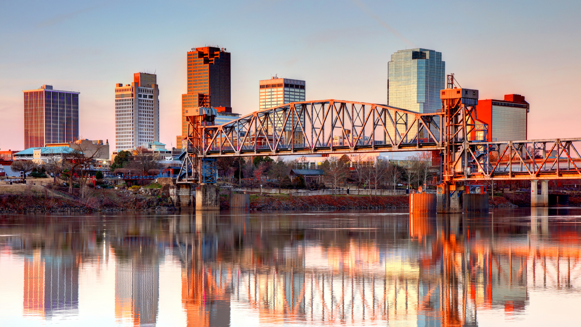 A bridge over a body of water with a Little Rock skyline in the background.