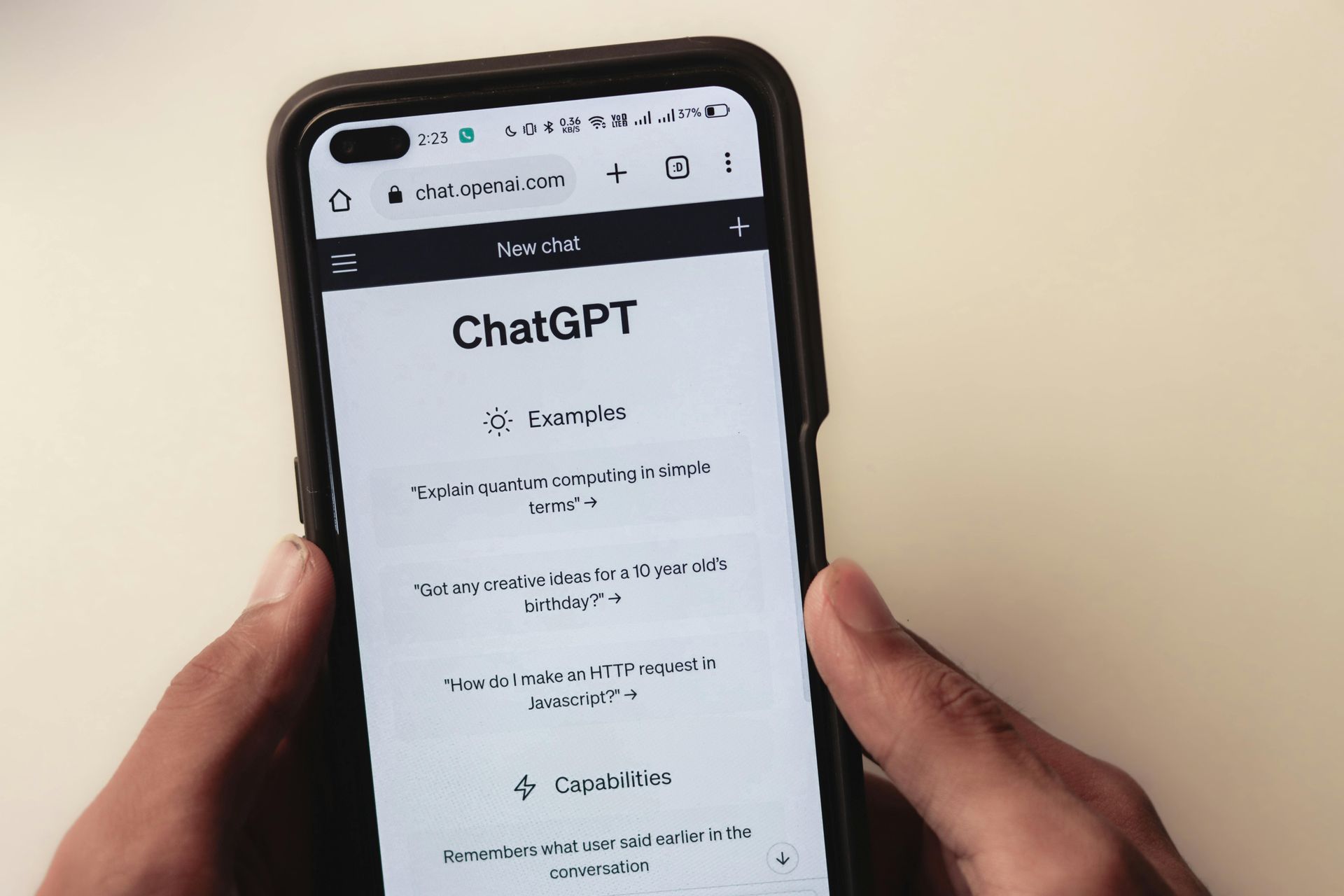 Hands holding a smartphone displaying the ChatGPT website on a light background.